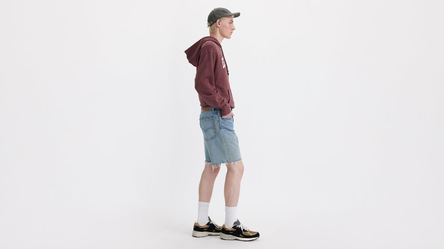 Side view of man in Levi’s 468 loose Shorts with maroon hoodie, cap, & sneakers