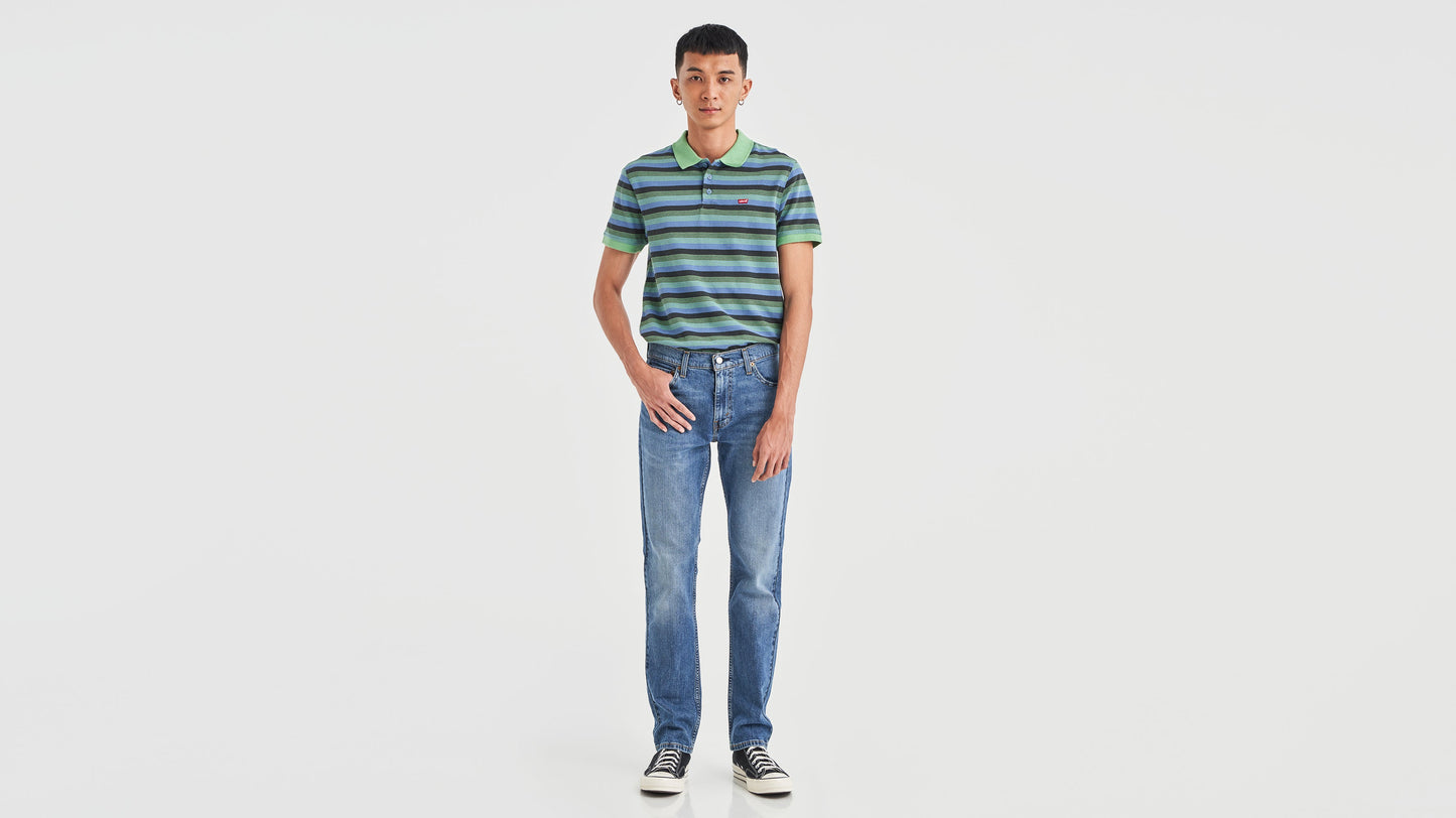 Front view of a man in striped green polo shirt, blue Levi’s 511 jeans, & sneakers