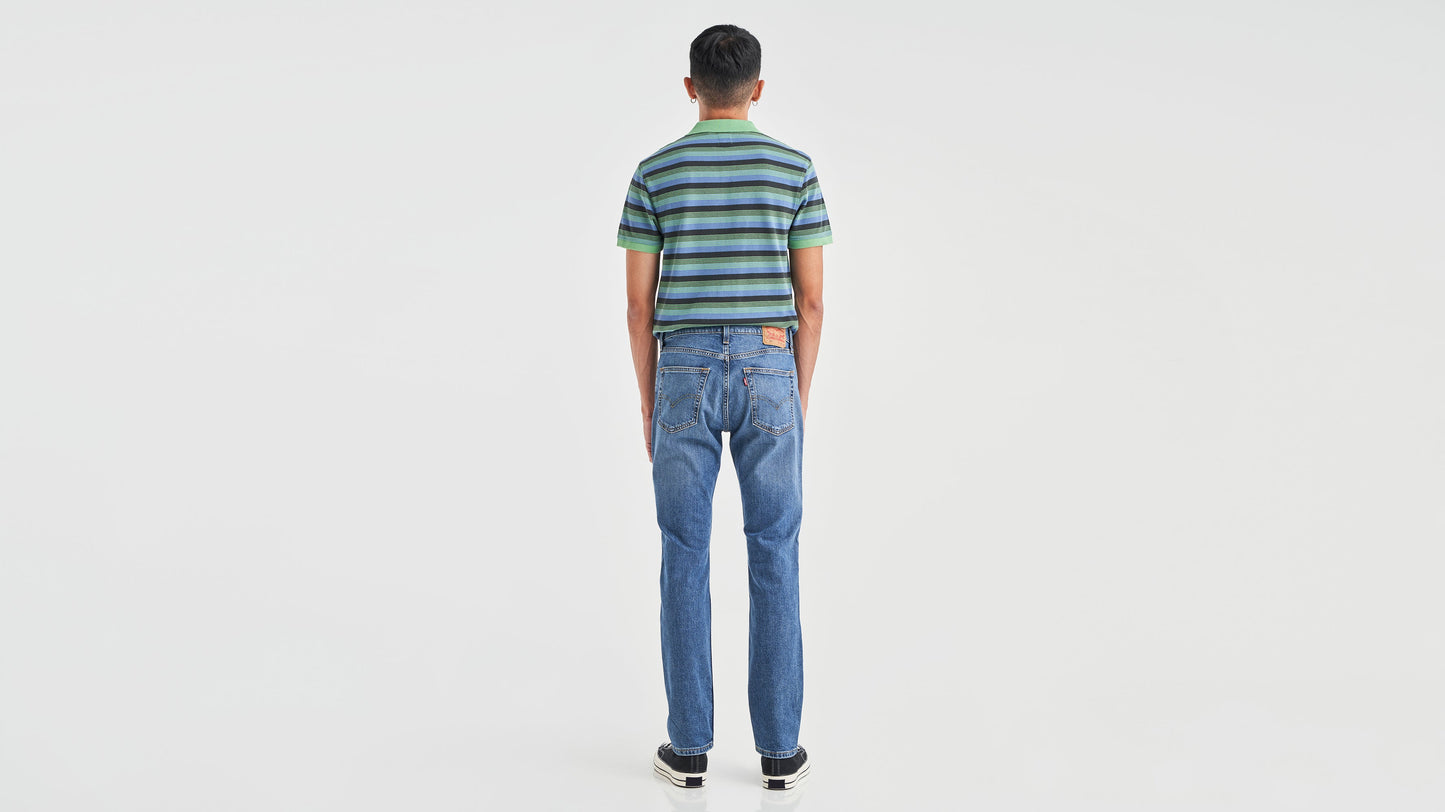 Back view of a man in striped green polo shirt, blue Levi’s 511 jeans, & sneakers