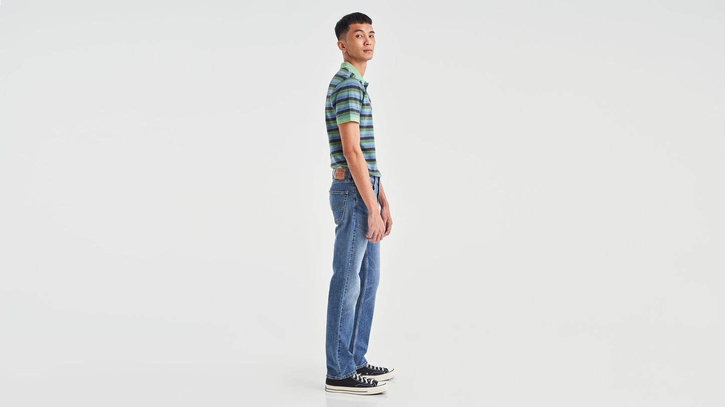 Side view of a man in striped green polo shirt, blue Levi’s 511 jeans, & sneakers