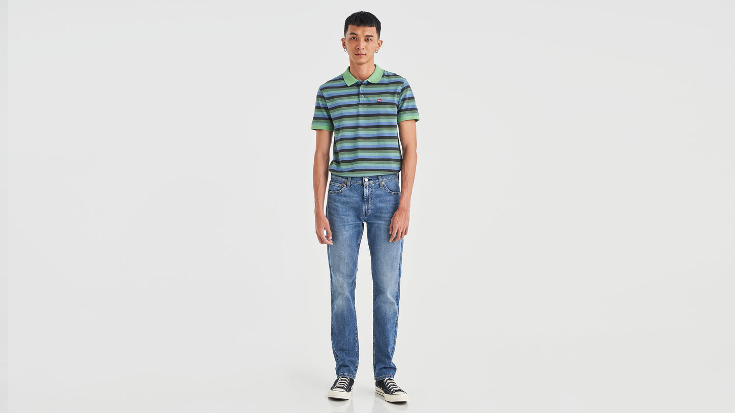 Front view of a man in green striped polo shirt, medium blue Levi’s 511 jeans, & sneakers