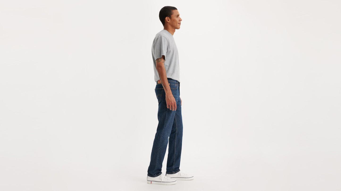 Side view of man in Levi’s 511 Slim Jeans in dark blue, grey tee, & white sneakers