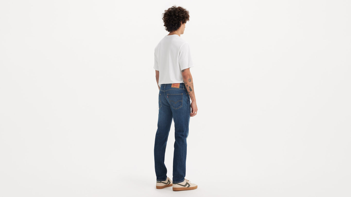 Back view of a man wearing mid-wash Levi’s 511 jeans with a white tee & sneakers