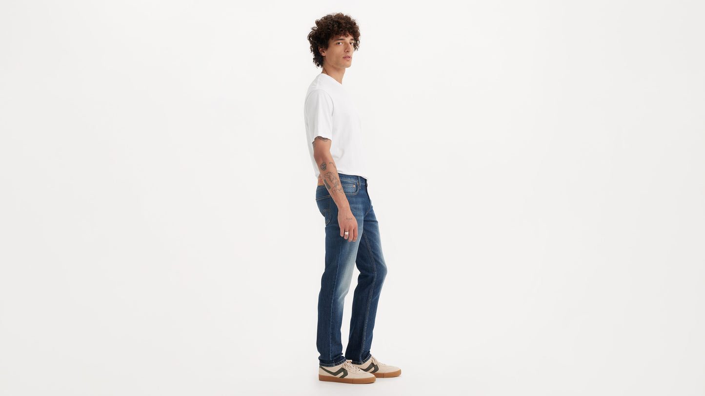 Side view of a man wearing mid-wash Levi’s 511 jeans with a white tee & sneakers