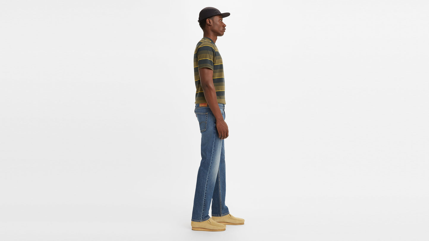 Side view of a man wearing mid-wash Levi’s 514 jeans with a striped shirt & shoes