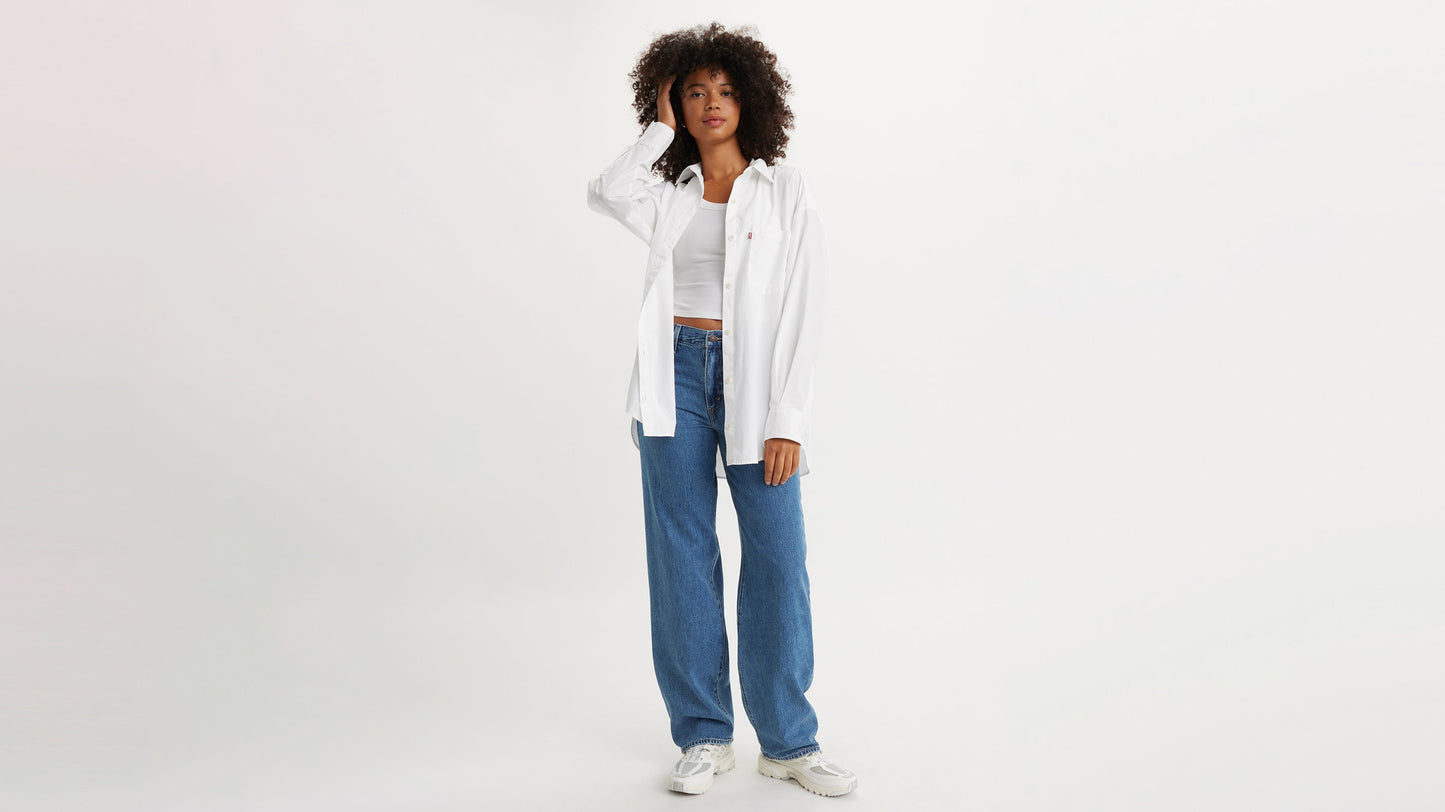 Woman poses in white button-up shirt & blue Levi's Baggy Jeans