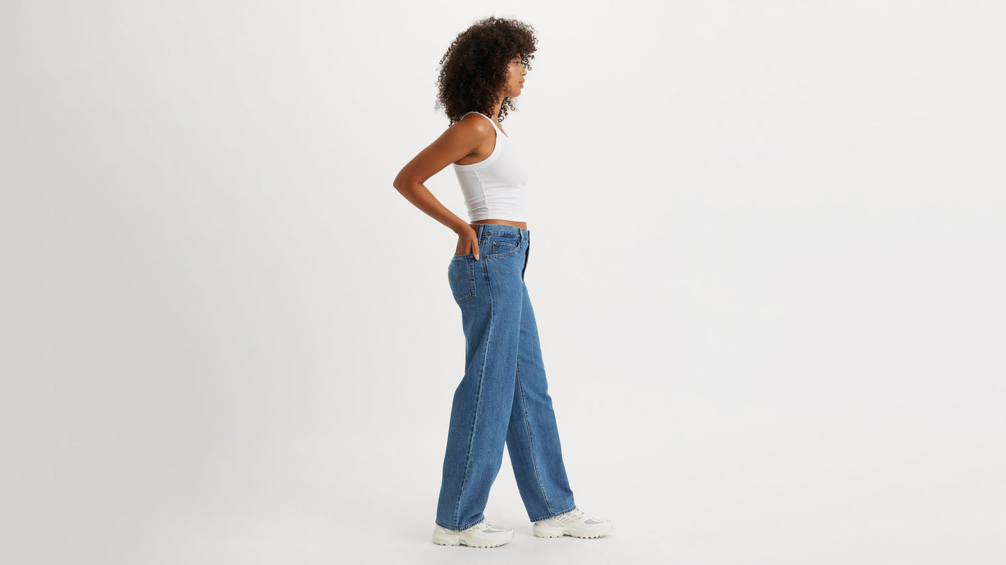 Side view of a woman in blue Levi's Baggy Jeans, white tank, & sneakers