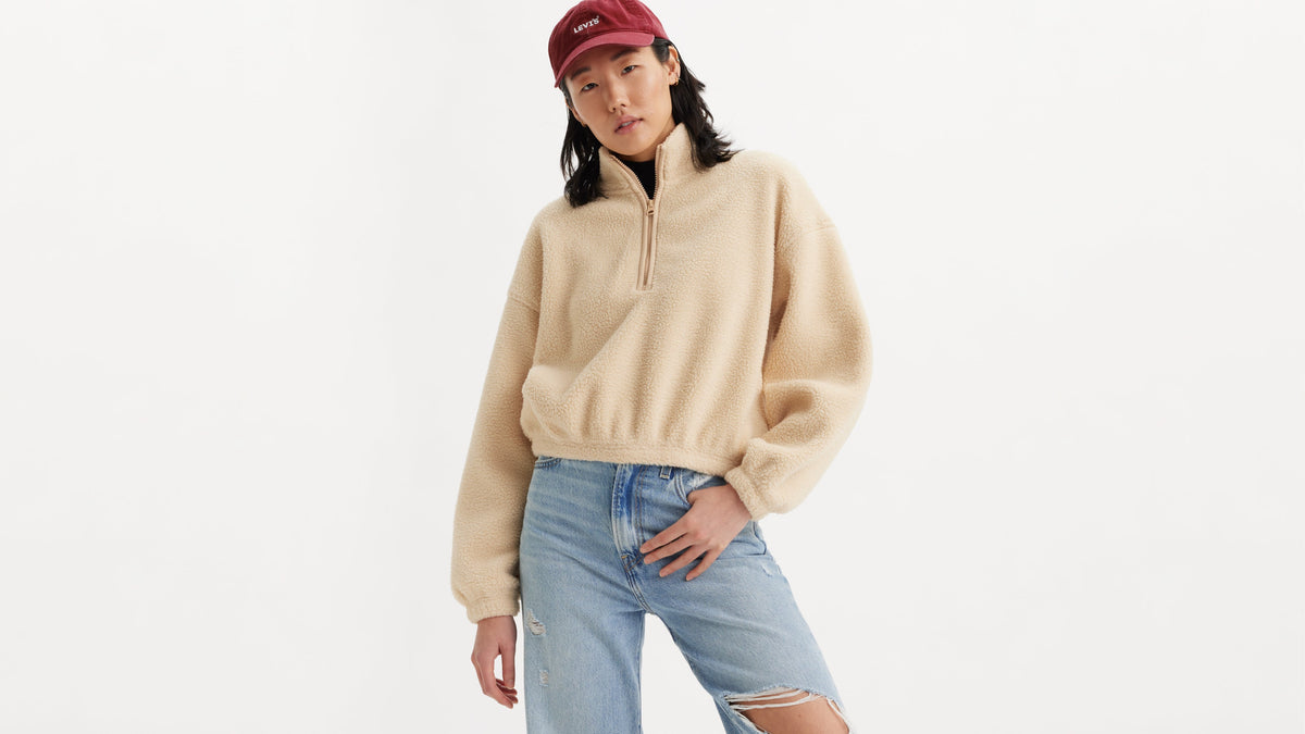 Woman wearing a beige quarter-zip sweater and red cap