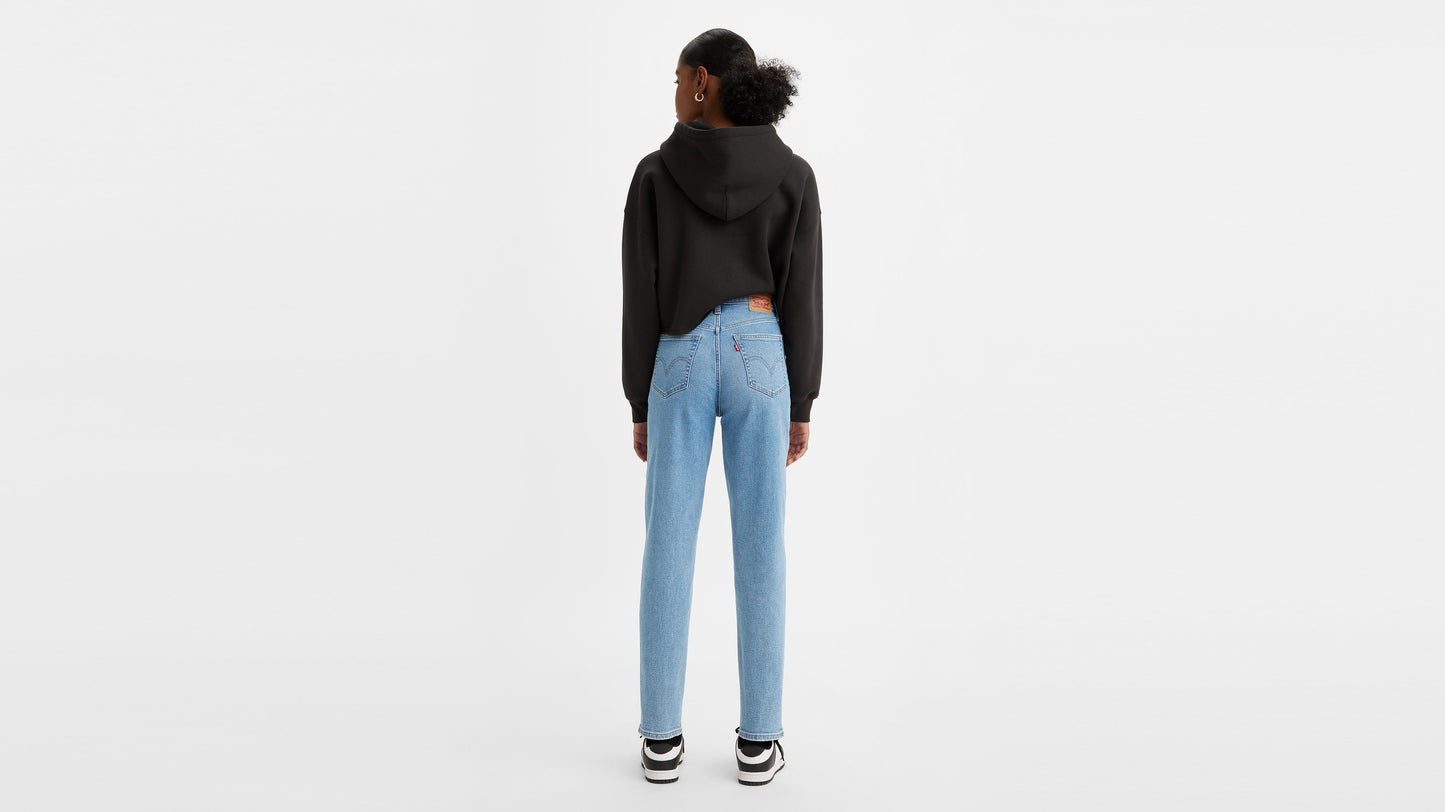 Woman in light wash high-waisted jeans, black hoodie, & sneakers, back view