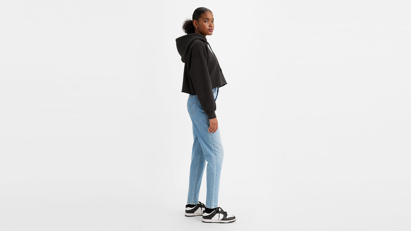 Side view of a woman in light wash high-waisted jeans, black hoodie, & sneakers