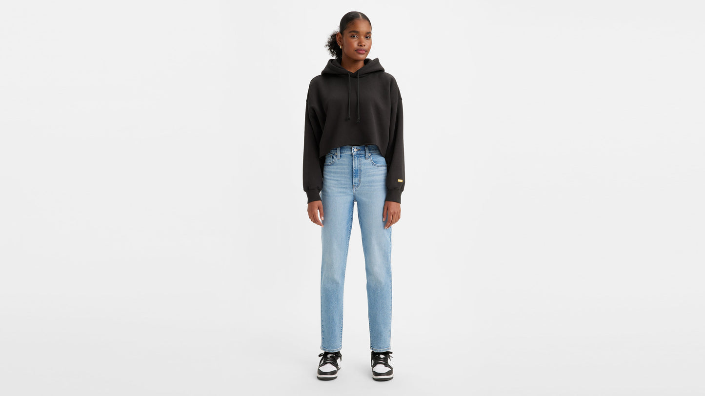Front view of a woman in cropped black hoodie, light wash high-waisted jeans, & sneakers