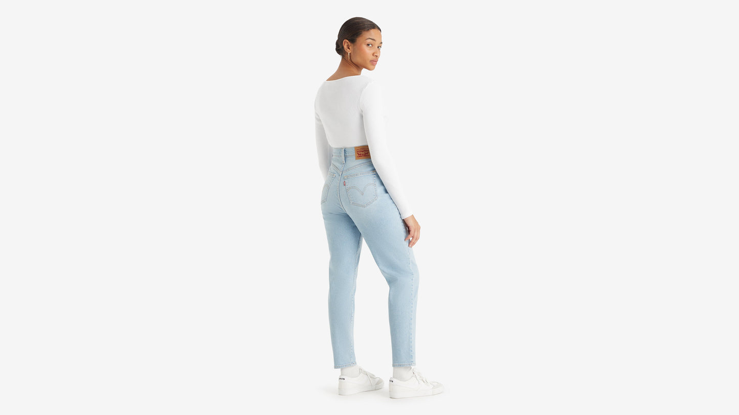 Back view of a woman in white top, sneakers, & high-waisted mom jeans