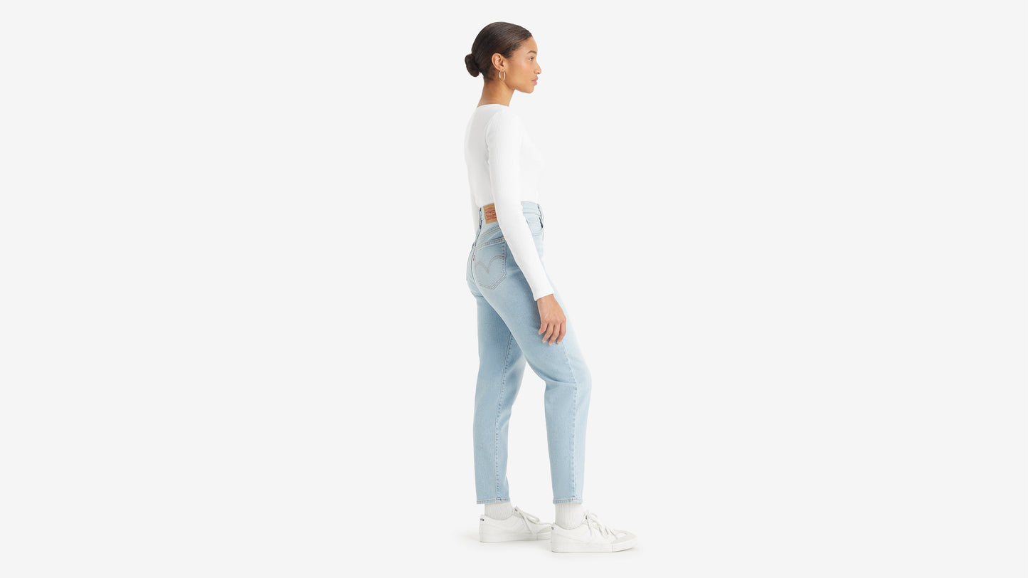 Side view of a woman in white top, sneakers, & high-waisted mom jeans