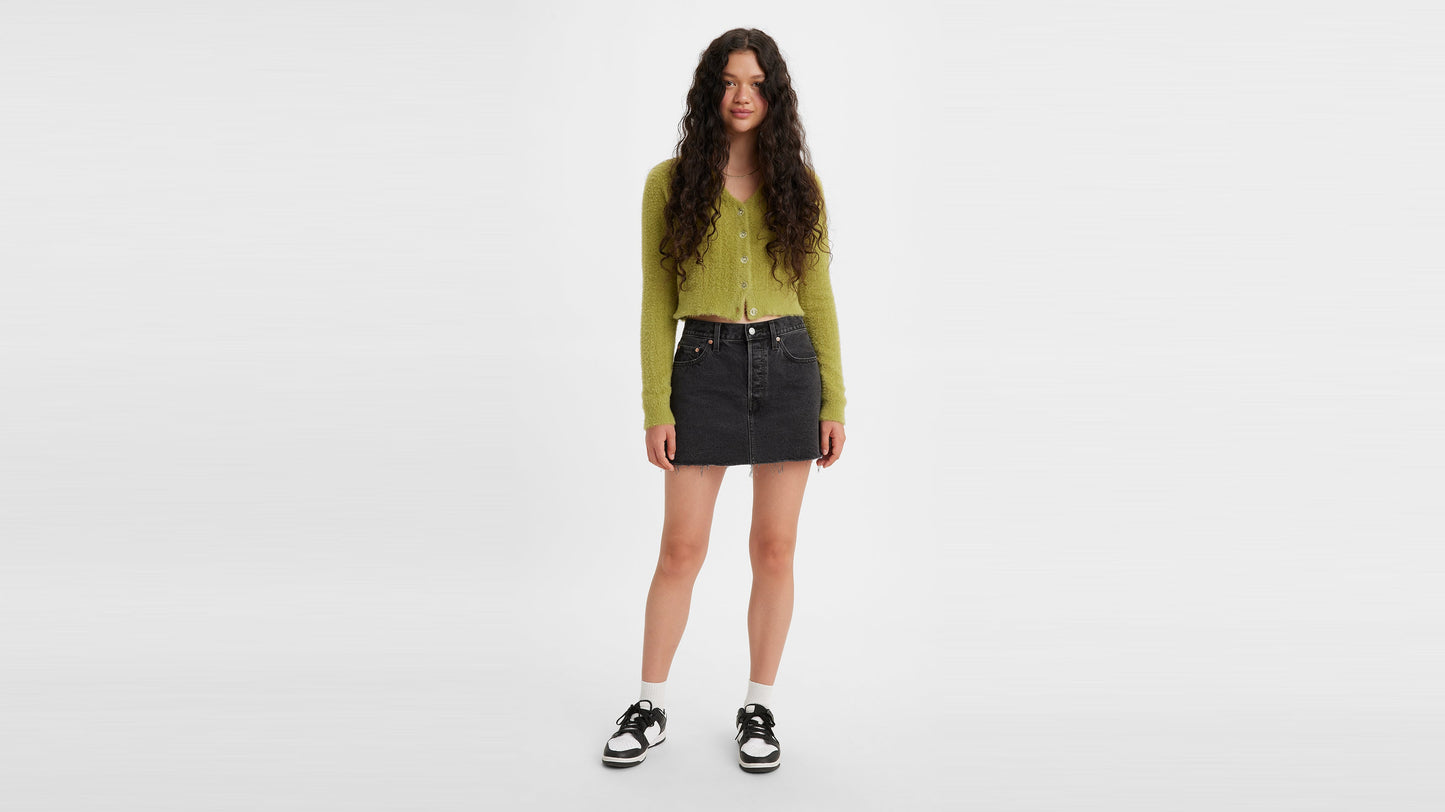 Front view of woman in black Levi's icon skirt with green cardigan and sneakers