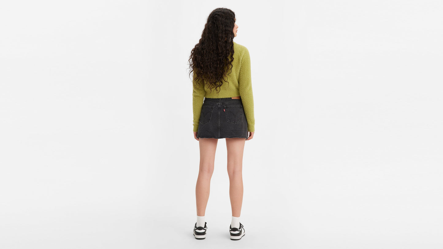 Back view of woman in black Levi's icon skirt with green cardigan and sneakers