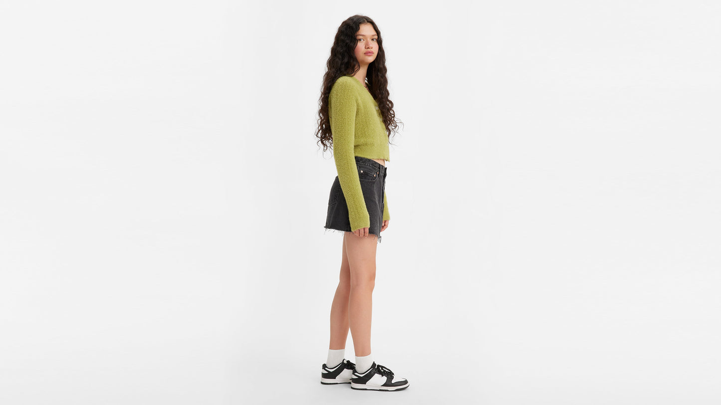 Side view of woman in black Levi's icon skirt with green cardigan and sneakers