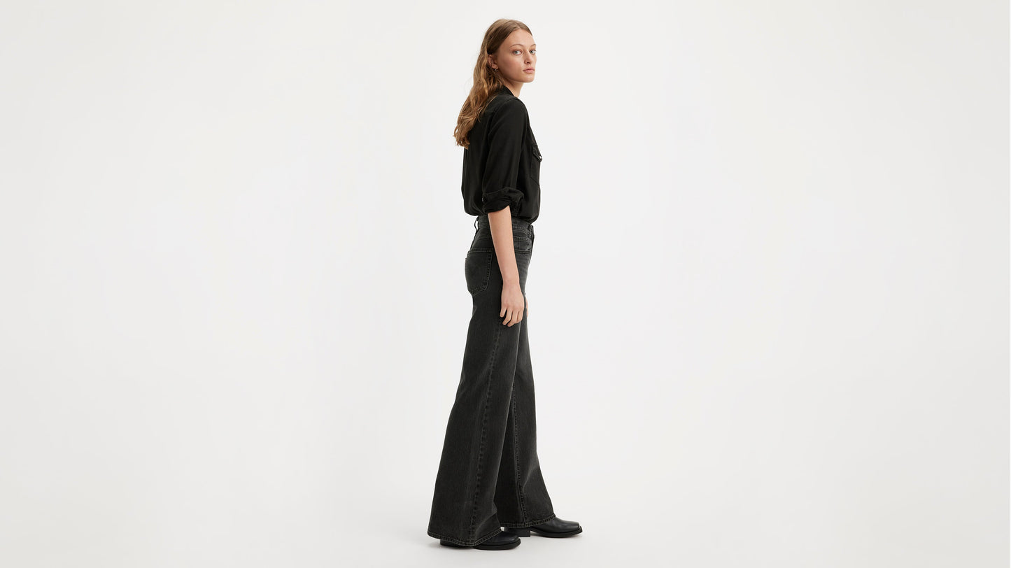 Side view of model in a black shirt & Levi's ribcage bell jeans, & black shoes