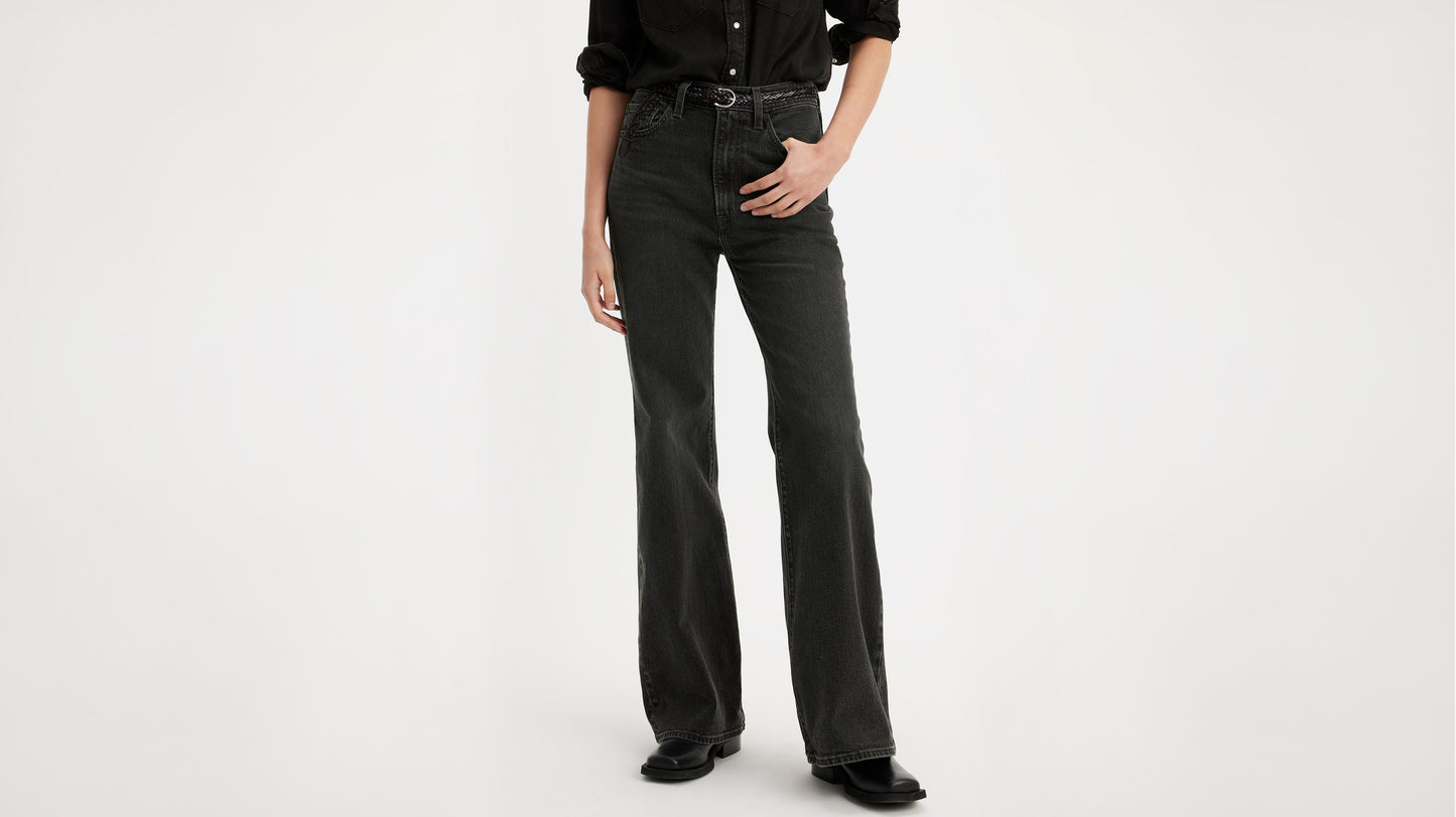 Half-body shot of a woman in black Levi's bell jeans, black belt, & black shoes