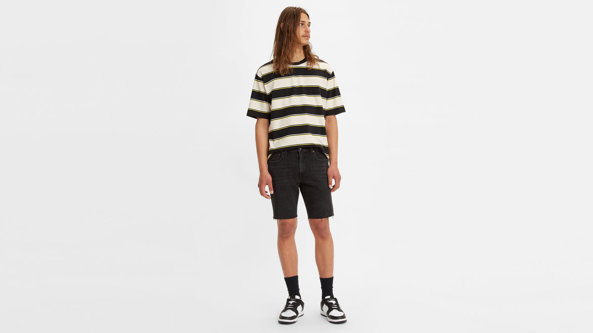 Front view of model in a striped t-shirt, black 412 Slim shorts, socks, & sneakers