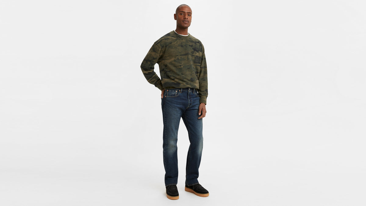 Angled full-body view of man in camo crewneck & dark 501 jeans