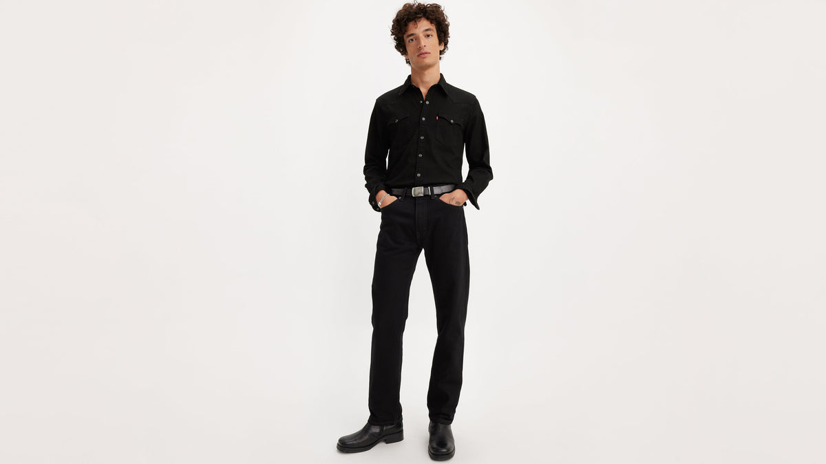 Front view of man wearing Levi’s 505 black jeans, black button shirt, belt, & boots