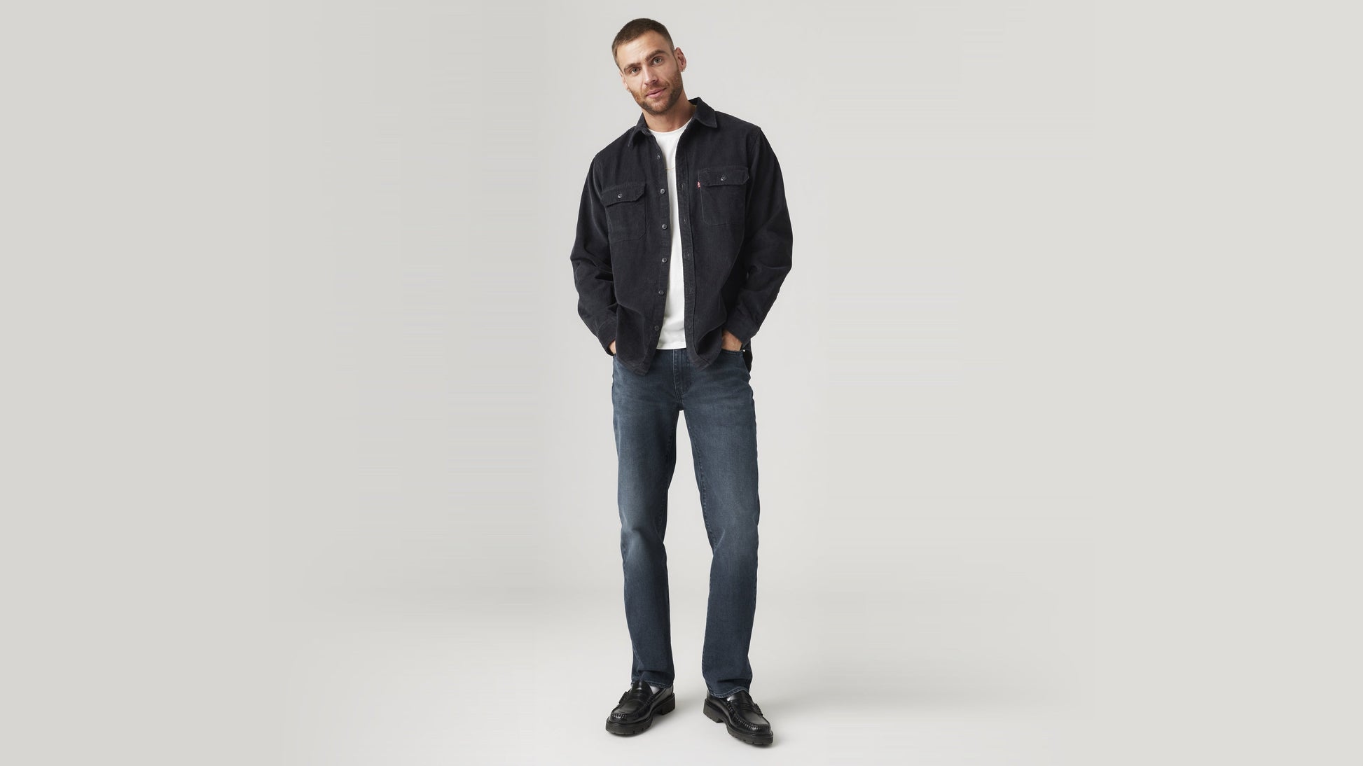 Front view of a man wearing dark wash Levi’s 514 jeans with a black overshirt & loafers