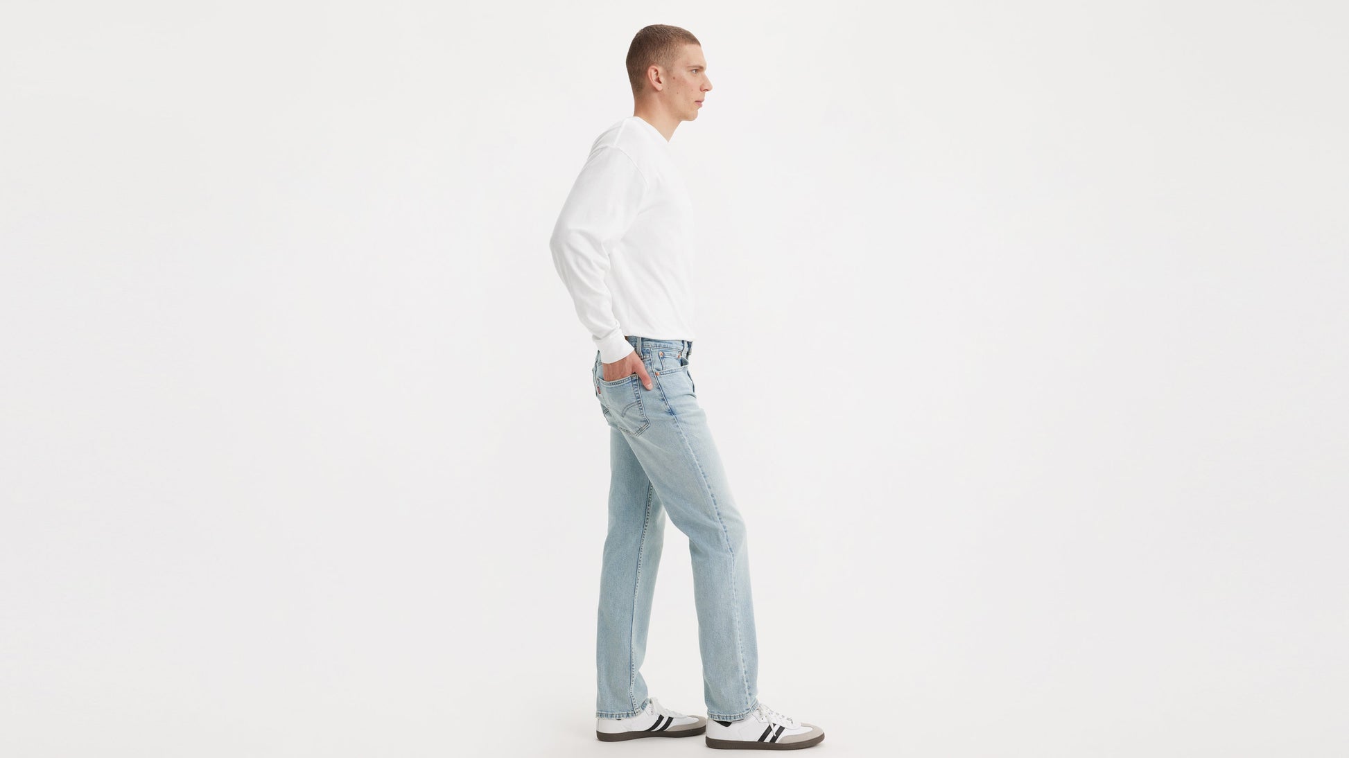Side view of a model in Levi’s Straight jeans, white long-sleeve shirt, & sneakers
