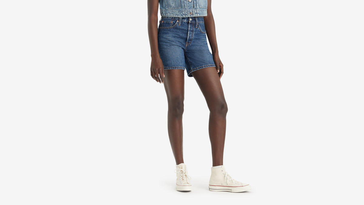 Half-body of a woman in Levi's 501 mid-thigh shorts with white sneakers