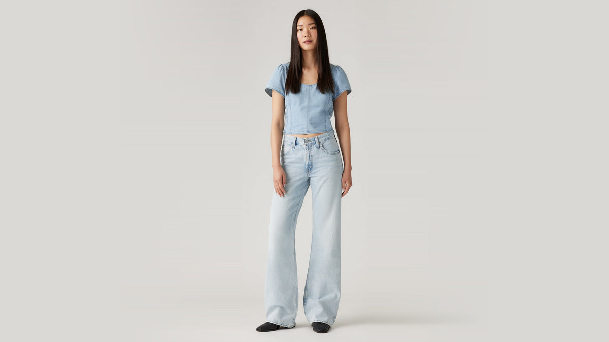 Front view of a woman in light blue Levi's Bootcut jeans & a cropped denim top