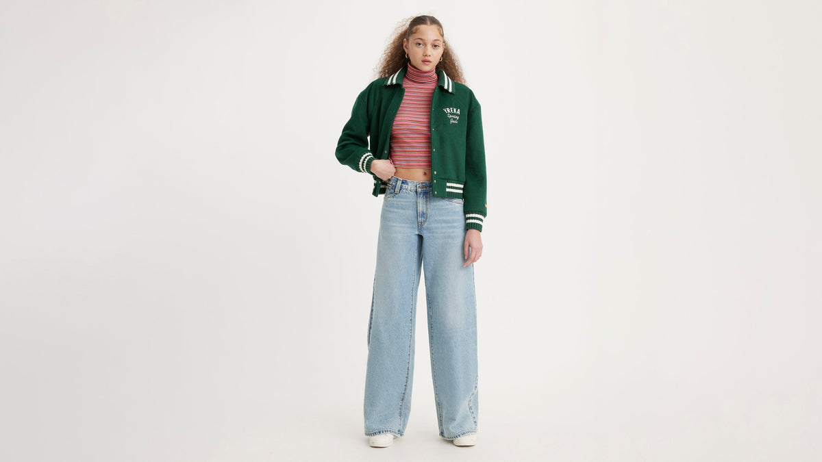 Woman in wide-leg jeans styled with a striped turtleneck & green varsity jacket