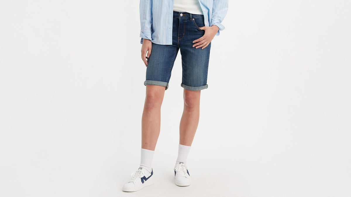 Half-body shot of a woman in dark Levi’s classic shorts, striped shirt, & sneakers