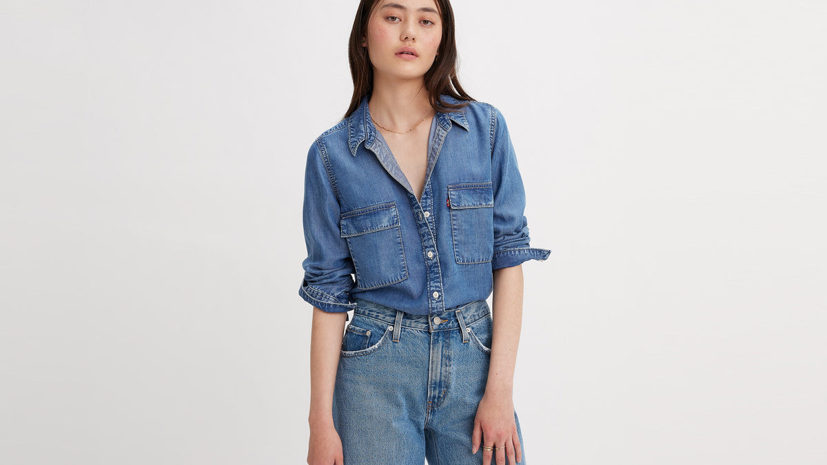 Model in blue button-up denim Doreen shirt tucked into high-waisted jeans, front view