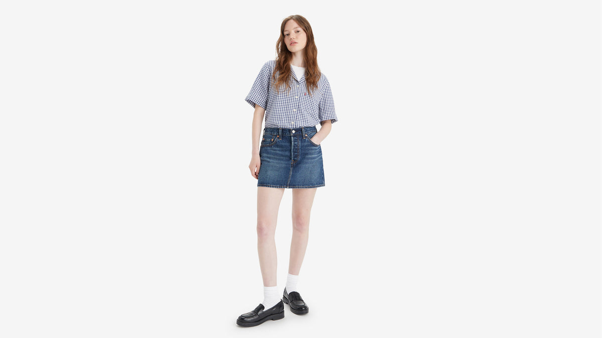 Front view of a woman in a Levi's Women's Icon Skirt, checked shirt, and loafers