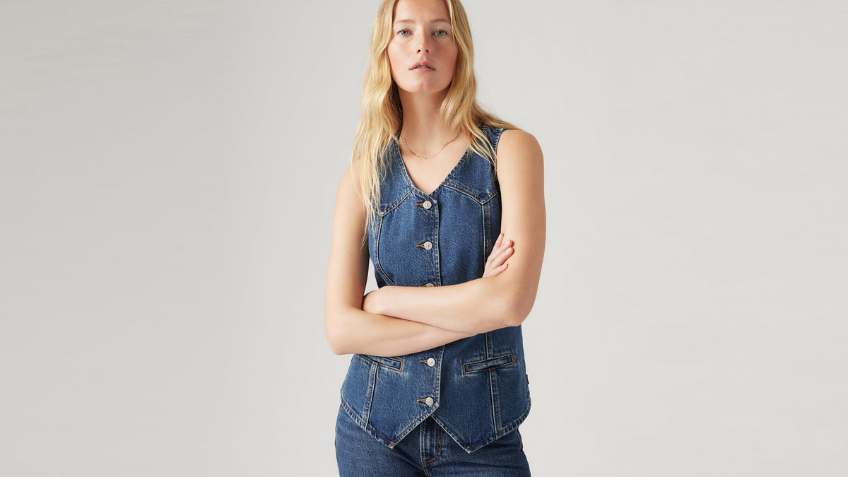 Front view of woman in button-up longline denim vest with jeans, crossed arms
