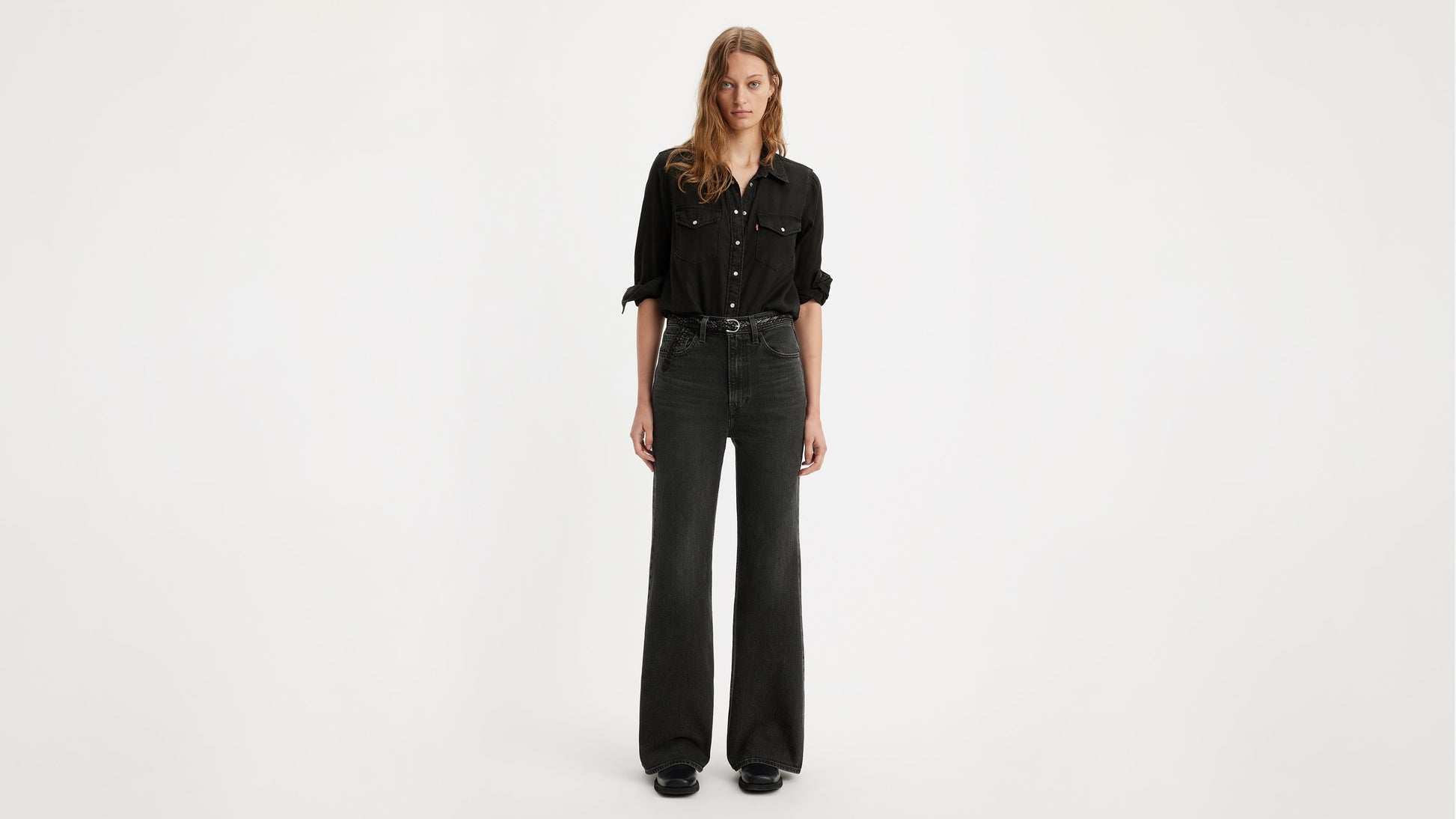 Model in a black shirt tucked into Levi's ribcage bell jeans with black belt