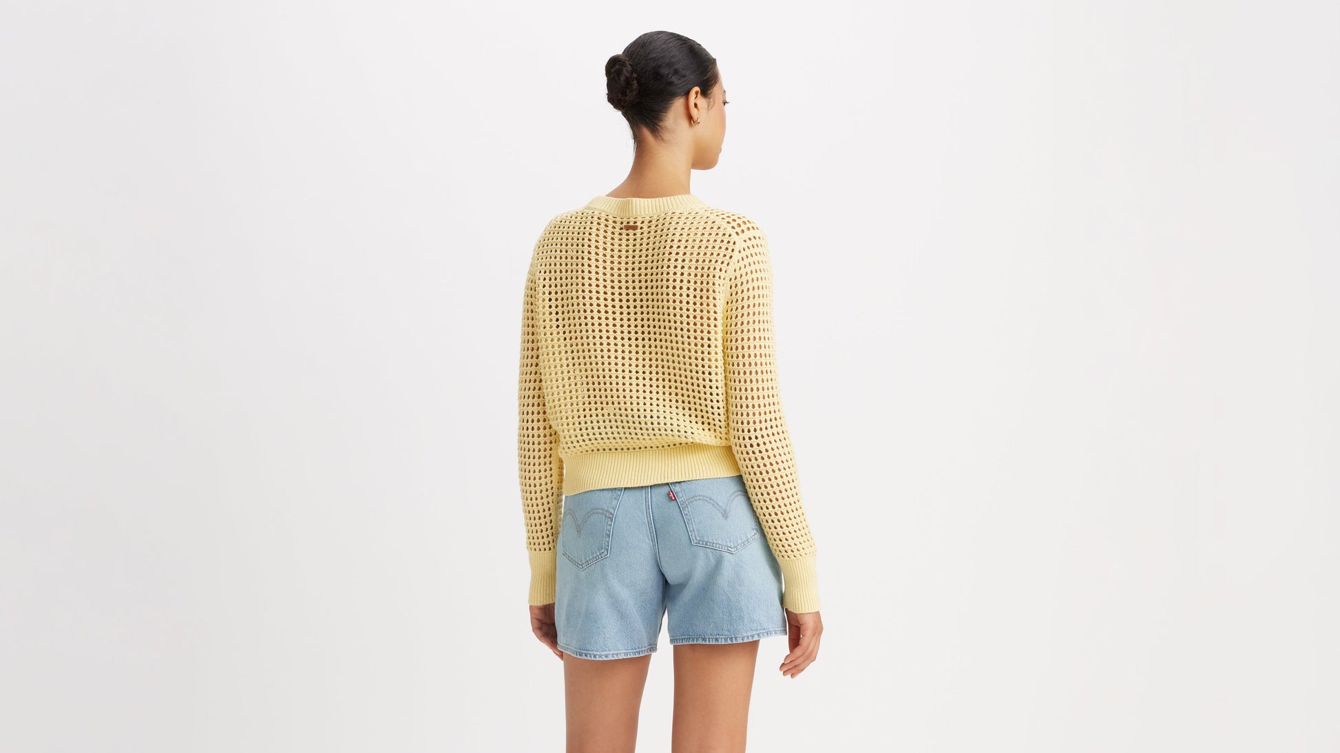 Back of model in yellow crochet sweater and denim shorts