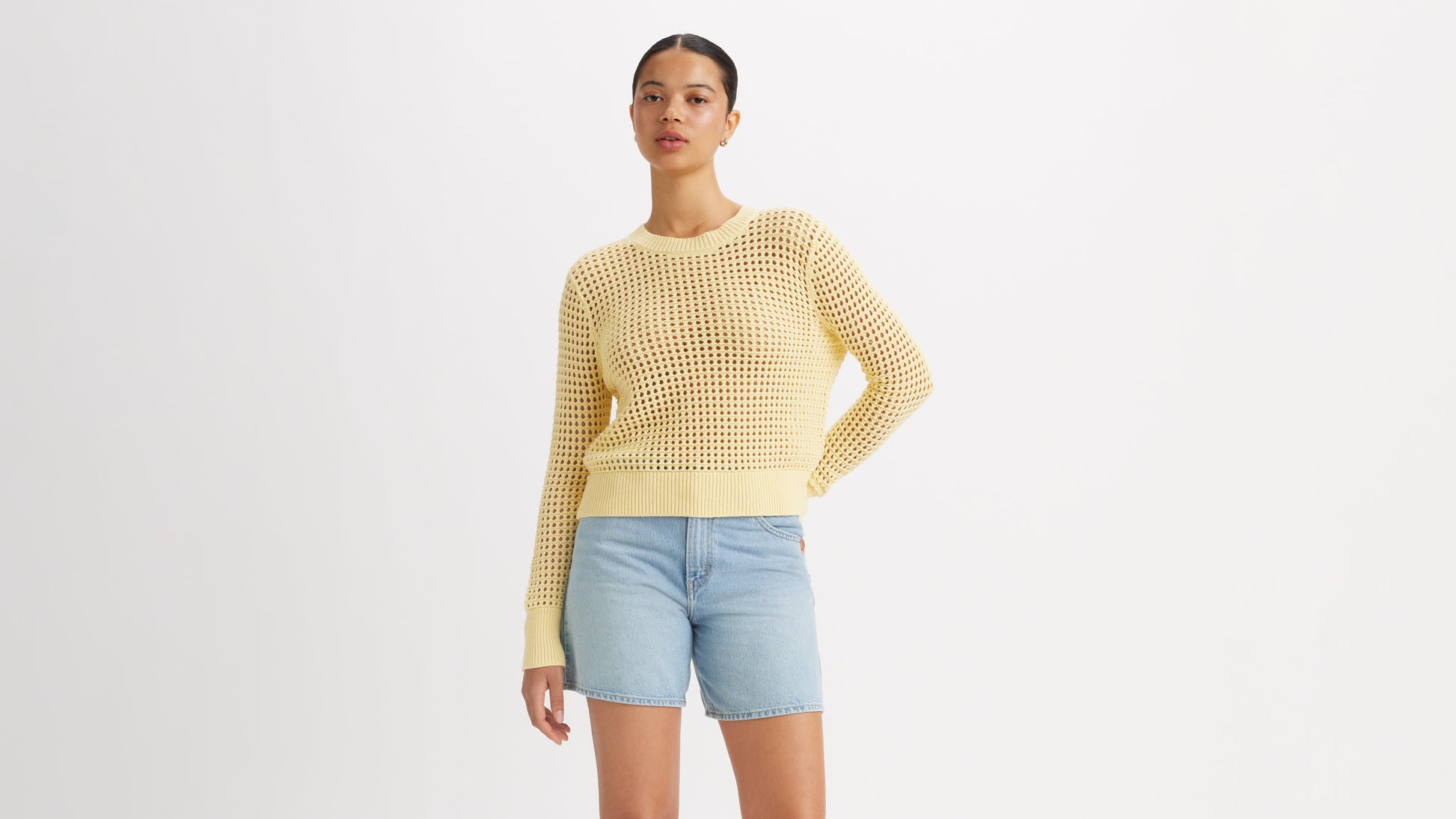 Model in light yellow crochet sweater and denim shorts