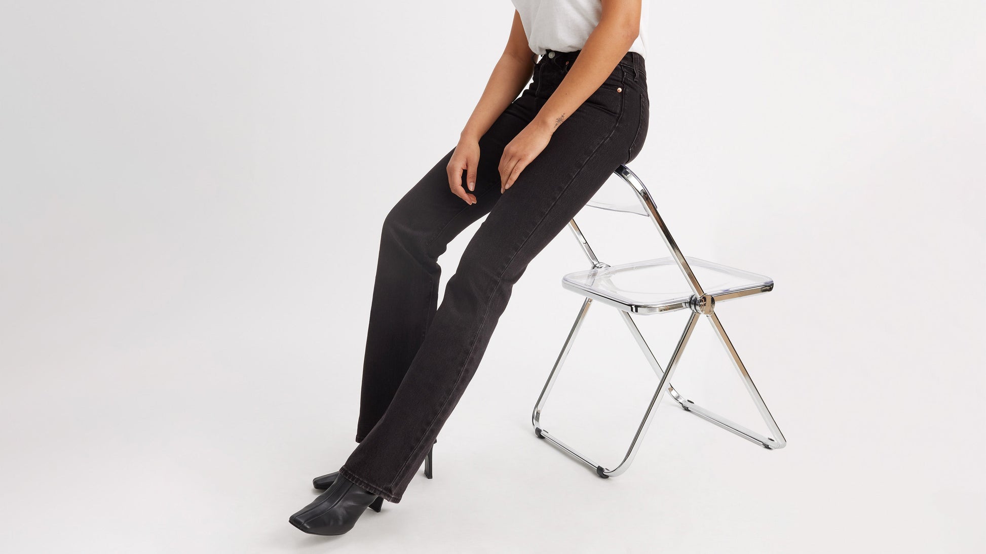 Cropped side view of a woman in black Levi's Wedgie Jeans, & boots, worn seated